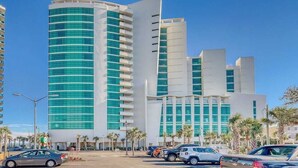 Um edifício moderno com fachada curva, várias varandas e um estacionamento com carros.