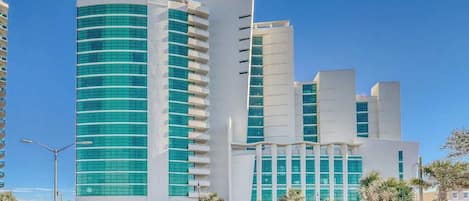 A modern building with a curved facade, multiple balconies, and a parking area with cars.