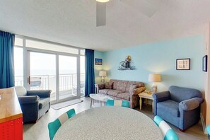 A room with a dining table, two sofas, a chair, a lamp, and a window with curtains. - Bay Watch Resort 0811 (North Myrtle Beach)