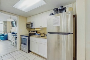 A compact kitchen with white cabinets, a stainless steel refrigerator, a microwave, and a stove. - Bay Watch Resort 1438 (North Myrtle Beach)