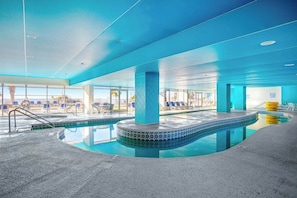 Ein Hallenbad mit blau gefliestem Rand, umgeben von Liegestühlen und freiem Blick ins Freie.