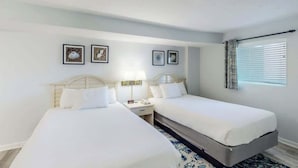 A hotel room with two beds, a nightstand, and a window with curtains. - Bay Watch Resort 0715 (North Myrtle Beach)