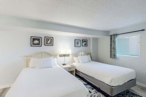 A hotel room with two beds, a nightstand, and a window with curtains. - Bay Watch Resort 0715 (North Myrtle Beach)