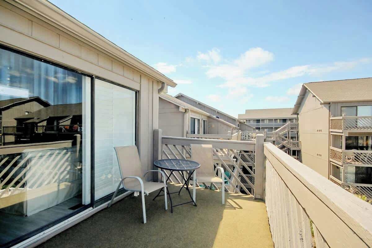 A balcony with a table and chairs, a glass door, and a view of adjacent buildings.