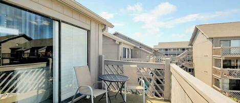 A balcony with a table and chairs, a glass door, and a view of adjacent buildings.