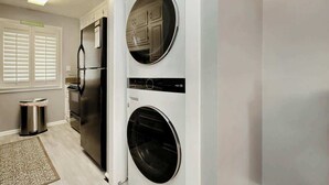 Eine kleine Küche mit Kühlschrank, Waschmaschine und Mülleimer.
