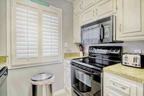 A kitchen with white cabinets, a stainless steel trash can, a microwave, a stove, and a toaster. - Shipwatch Pointe I - C303 (Myrtle Beach)