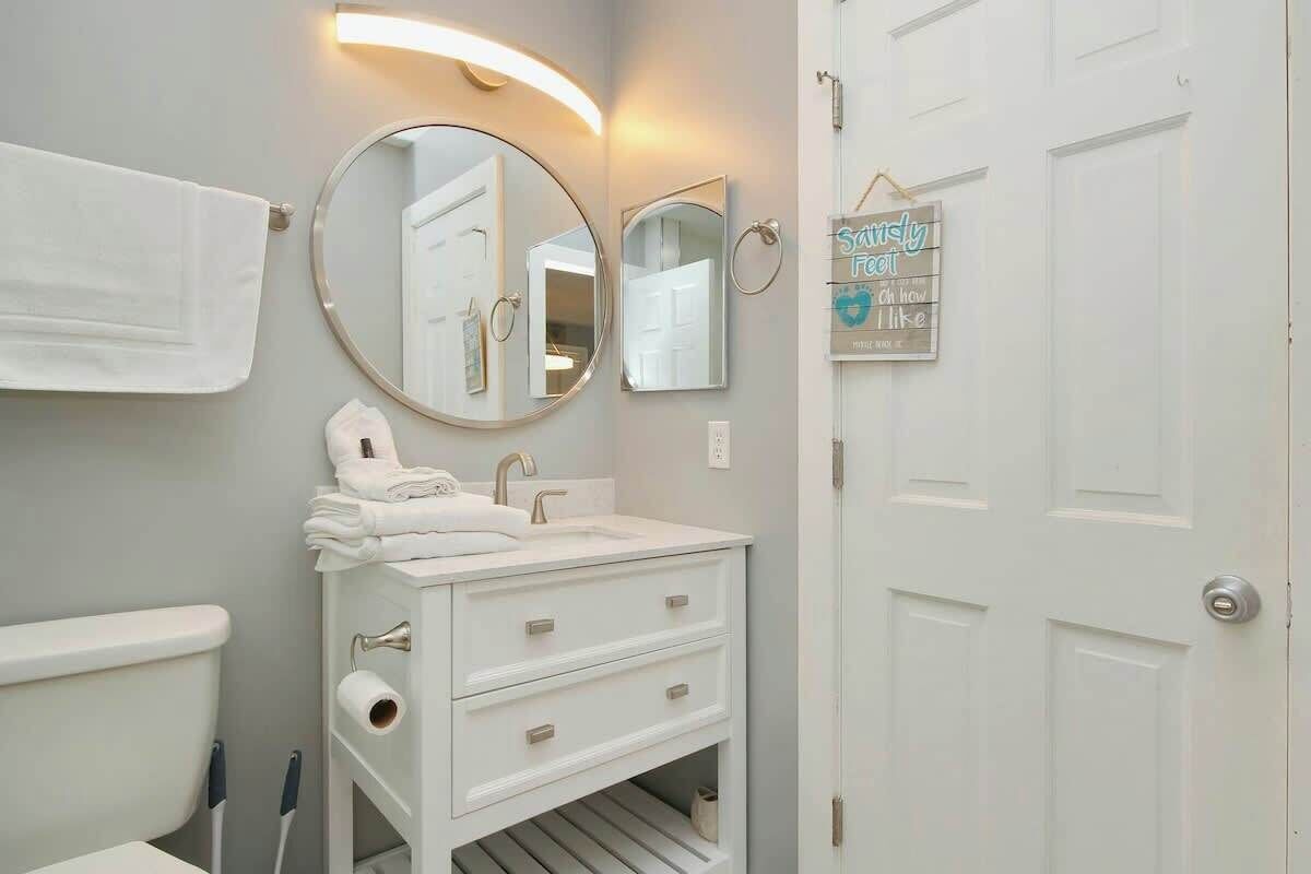 A bathroom with a white sink, a round mirror, a towel rack, and a door with a sign.