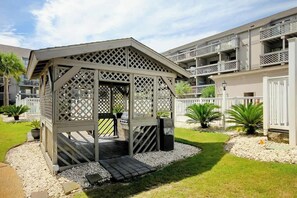 A covered outdoor seating area with a lattice design, surrounded by a white fence and potted plants. - Shipwatch Pointe I - C303 (Myrtle Beach)
