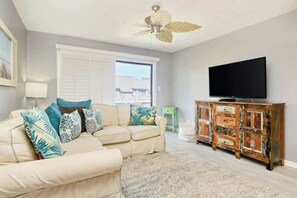 A living room with a beige sofa, patterned cushions, a television, and a decorative cabinet. - Shipwatch Pointe I - C303 (Myrtle Beach)