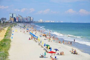 Ein Strand mit einer Mole, Menschen und Gebäuden im Hintergrund.