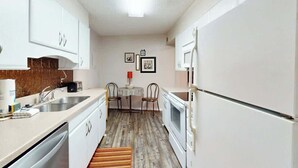 A compact kitchen with white cabinets, a sink, a stove, and a microwave. There is a small dining table with chairs. - Sea and Sails Retreat (Myrtle Beach)