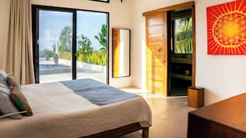 A modern bedroom with a large bed, a sliding glass door leading to a balcony, and a wooden door to a bathroom.