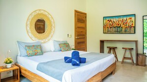 Ein Schlafzimmer mit einem Bett, einem Wandspiegel, einer Holztür, einem Gemälde und einem kleinen Schreibtisch mit Hockern.