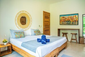 A bedroom with a bed, a wall-mounted mirror, a wooden door, a painting, and a small desk with stools. - VILLA HOLISTIKA: Ocean view, private pool, 6 bedrooms, El Portillo, Las Terrenas (Las Terrenas)