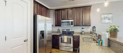 A modern kitchen with stainless steel appliances, dark wooden cabinets, granite countertops, and a built-in oven.