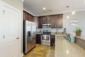 Eine moderne Küche mit Edelstahlgeräten, dunklen Holzausziehtüren, Granit Arbeitsplatten und einem eingebauten Backofen.
