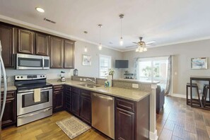 A modern kitchen with dark wood cabinets, stainless steel appliances, and a large island with a sink. - Kashton Charms Retreat (Myrtle Beach)