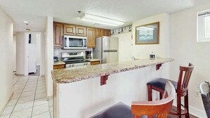 A kitchen with wooden cabinets, a microwave, a refrigerator, and a granite countertop. - Lighthouse Corner Getaway (Myrtle Beach)