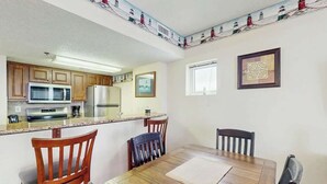 A kitchen with wooden cabinets, a microwave, and a refrigerator. There is a dining table with chairs and a window with a view of lighthouses. - Lighthouse Corner Getaway (Myrtle Beach)