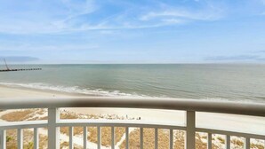 A beach view from a balcony with a railing, ocean, and distant shoreline. - Lighthouse Corner Getaway (Myrtle Beach)