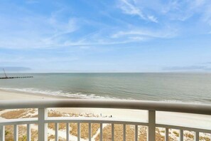 Vista da praia a partir de uma varanda com guarda-corpo, oceano e costa distante.