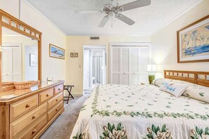 Ein Schlafzimmer mit Bett, Kommode, Spiegel, Deckenventilator und einem Bild an der Wand.