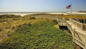 En träpromenad som leder till en strand där en amerikansk flagga vajar.