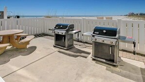 En uteplats med två grillar, ett picknickbord och ett vitt staket.