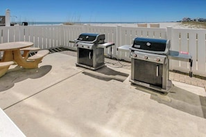 An outdoor patio with two barbecue grills, a picnic table, and a white fence. - Sands Beach Club 1015 - Bright Shores (Myrtle Beach)