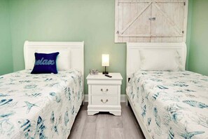 A room with two beds, each with a white headboard and a floral bedspread. There is a white nightstand between the beds with a lamp on it. - Sands Beach Club 1015 - Bright Shores (Myrtle Beach)