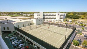 En tenniskort intill ett parkeringshus med flera våningar, med en byggnad synlig i bakgrunden.