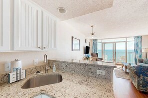 A kitchen with a granite countertop, a sink, and a dining area with a table and chairs. - Bay Watch Resort 1520 (North Myrtle Beach)