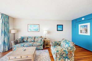 A living room with two floral-patterned sofas, a wooden coffee table, and a blue accent wall. - Bay Watch Resort 1520 (North Myrtle Beach)