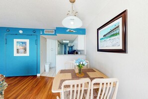 A room with a dining table, chairs, a vase with flowers, a ceiling fan, and a framed picture on the wall. - Bay Watch Resort 1520 (North Myrtle Beach)