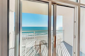 A balcony with a view of the sea, white chairs, and a glass door. - Bay Watch Resort 1520 (North Myrtle Beach)