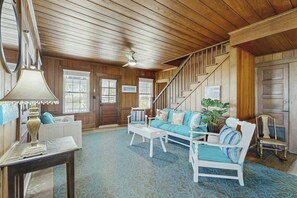 Ein Zimmer mit Holzbalkendecke, einer Treppe, einem blau gemusterten Teppich und einem weißen Sofa mit blauen Kissen.