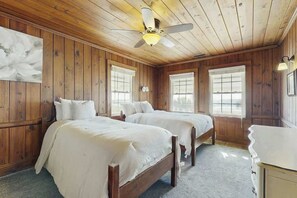 Ein Zimmer mit Holzwandverkleidung, zwei Betten mit weißer Bettwäsche, einem Deckenventilator und einem großen Fenster.