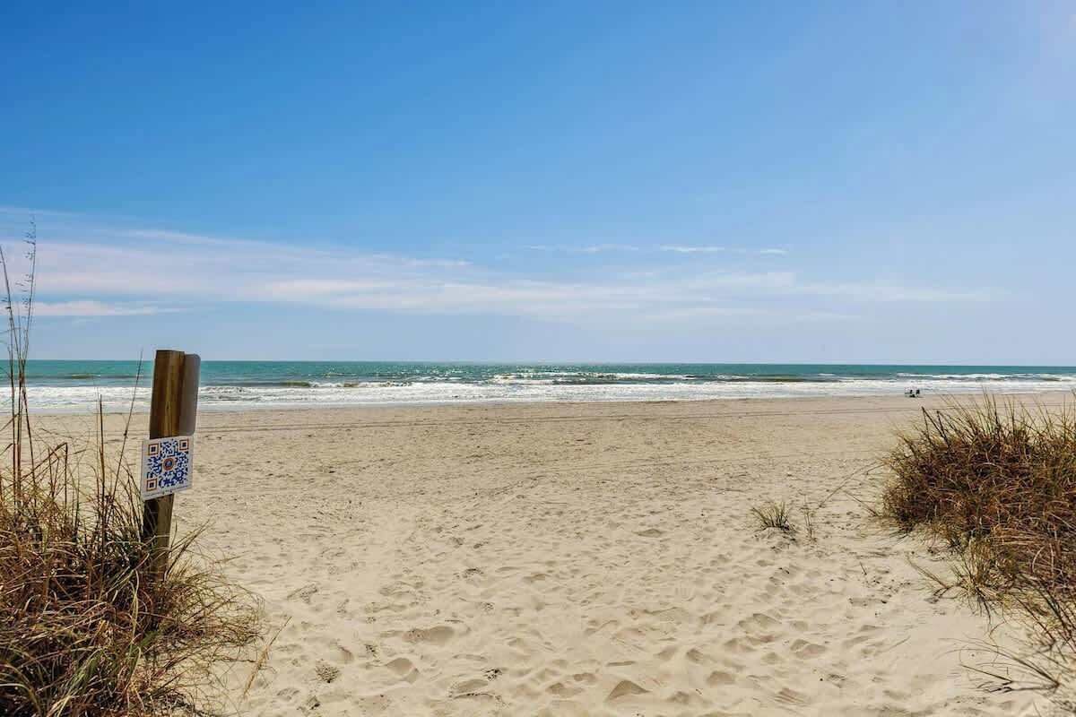 En sandstrand med en træpæl, der viser en QR-kode.