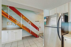 Eine Küche mit weißen Schränken, einem Edelstahlkühlschrank und einer Holztreppe.