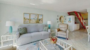 Un salon avec un canapé, des fauteuils, une table basse et un escalier en arrière-plan.