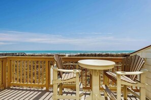 A wooden deck with a round table and two Adirondack chairs overlooking a beach. - Perfect Harmony Retreat (North Myrtle Beach)