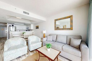 A modern living room with a sofa, two armchairs, a coffee table, and a large mirror on the wall. - Camelot by the Sea 0905 (Myrtle Beach)