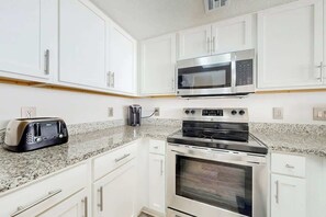 A kitchen with white cabinets, a microwave, a toaster, and a stove. - Camelot by the Sea 0905 (Myrtle Beach)