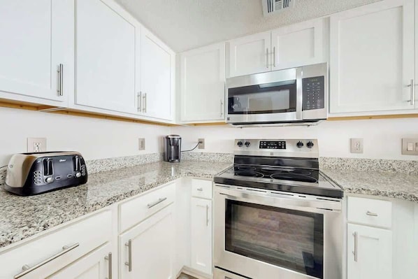 A kitchen with white cabinets, a microwave, a toaster, and a stove. - Camelot by the Sea 0905 (Myrtle Beach)