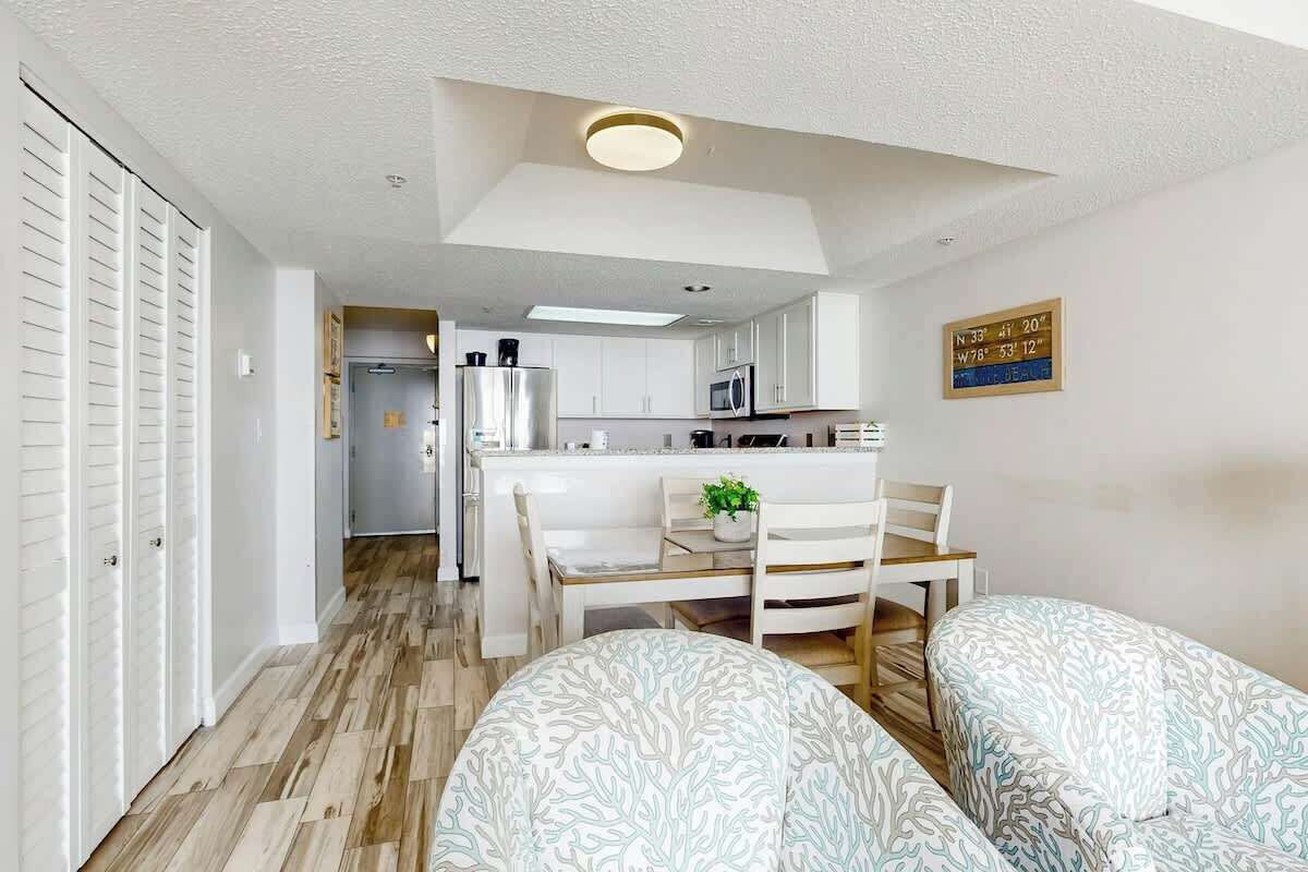 Un espacio habitable compacto con kitchenette, comedor con mesa y sillas, y una pequeña zona de estar con cojines estampados.