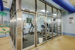 A gym with exercise equipment, a glass door entrance, and a wall mural. - Golden Mile Condo Retreat (Myrtle Beach)