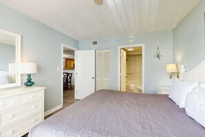 A bedroom with a bed, a dresser, a mirror, and a door leading to a bathroom. - Golden Mile Condo Retreat (Myrtle Beach)