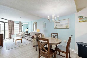 A living room with a dining table, chairs, a sofa, and a chandelier. - Golden Mile Condo Retreat (Myrtle Beach)