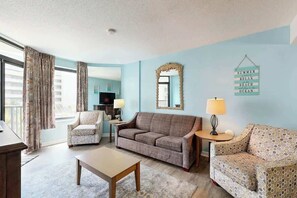 Ein Wohnzimmer mit einer Couch, Sesseln, einem Couchtisch und einem Fernseher.